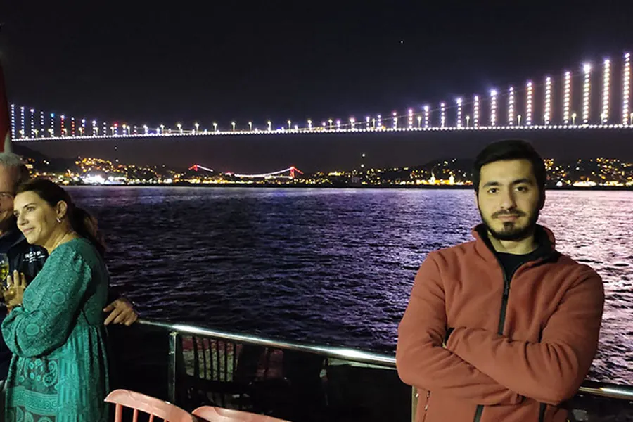 Invitados en cubierta frente al Puente del Bósforo iluminado de noche