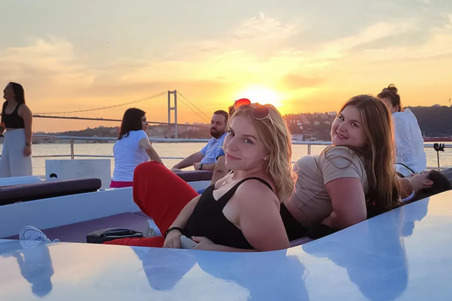 Guests relaxing on the bow of the yacht at sunset with the Bosphorus Bridge behind